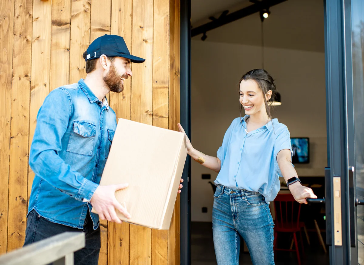 Happy twenty-something delivery customer accepts parcel on from driver on doorstep