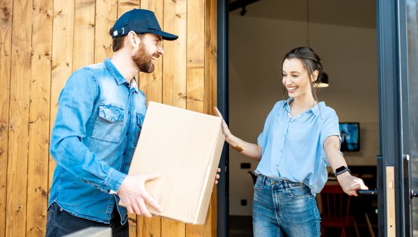 Happy twenty-something delivery customer accepts parcel on from driver on doorstep